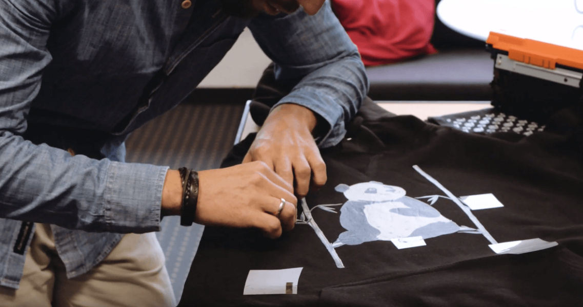 A man places transfer foil with white toner on a black hoodie